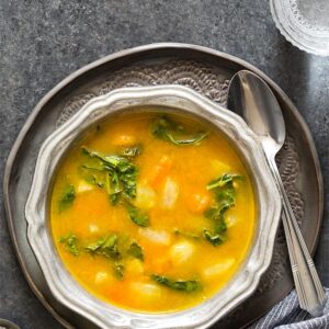 Kohlrabi Soup with Kohlrabi Greens in a silver ridged bowl on a dark gray plate