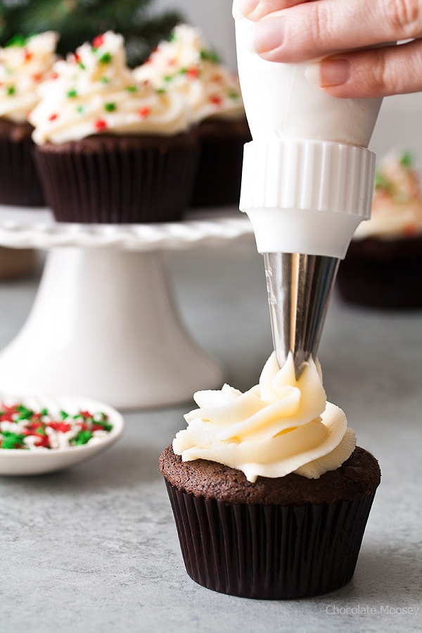 Piping cream cheese frosting on cupcakes