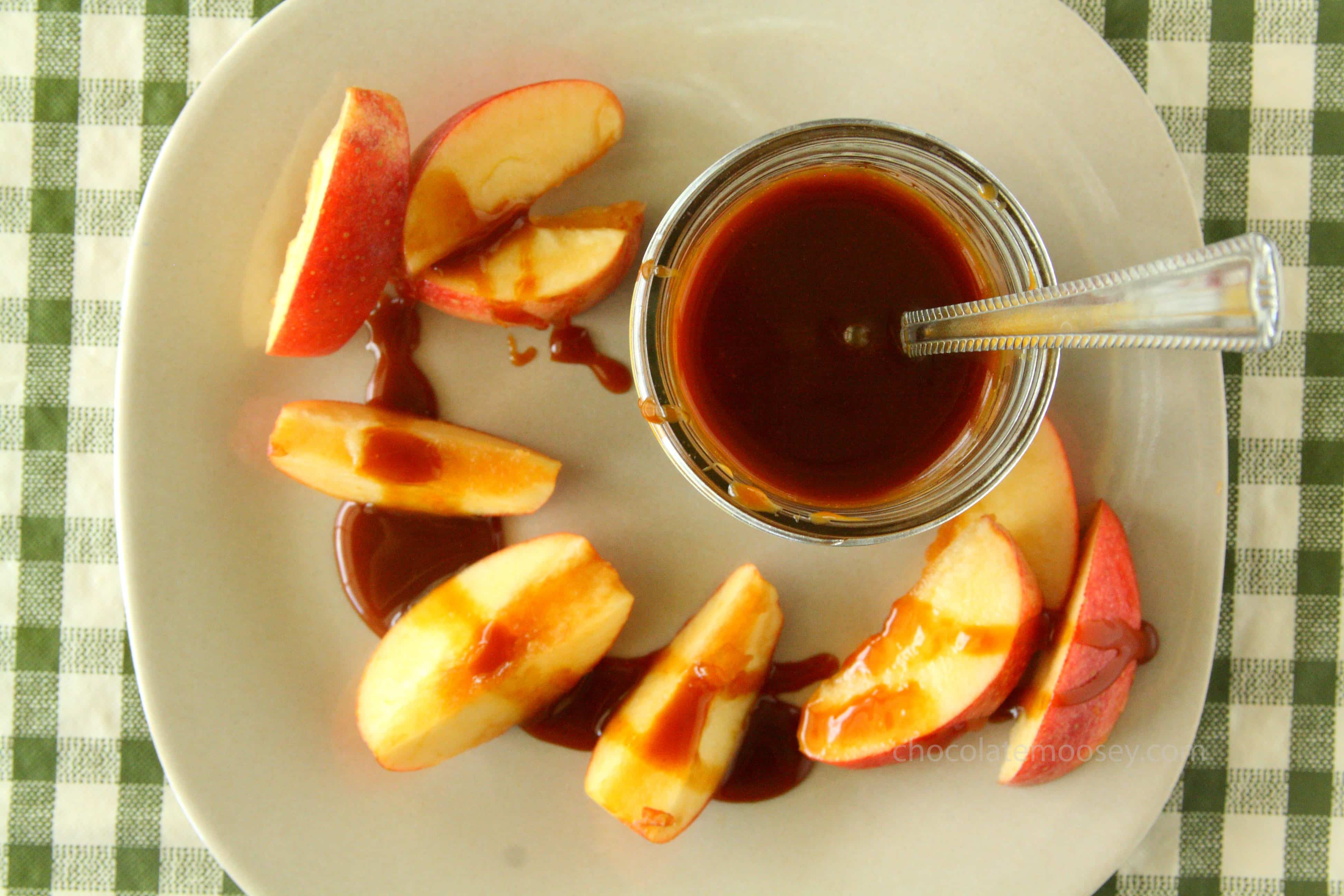 Jar of caramel sauce on plate with apple slices