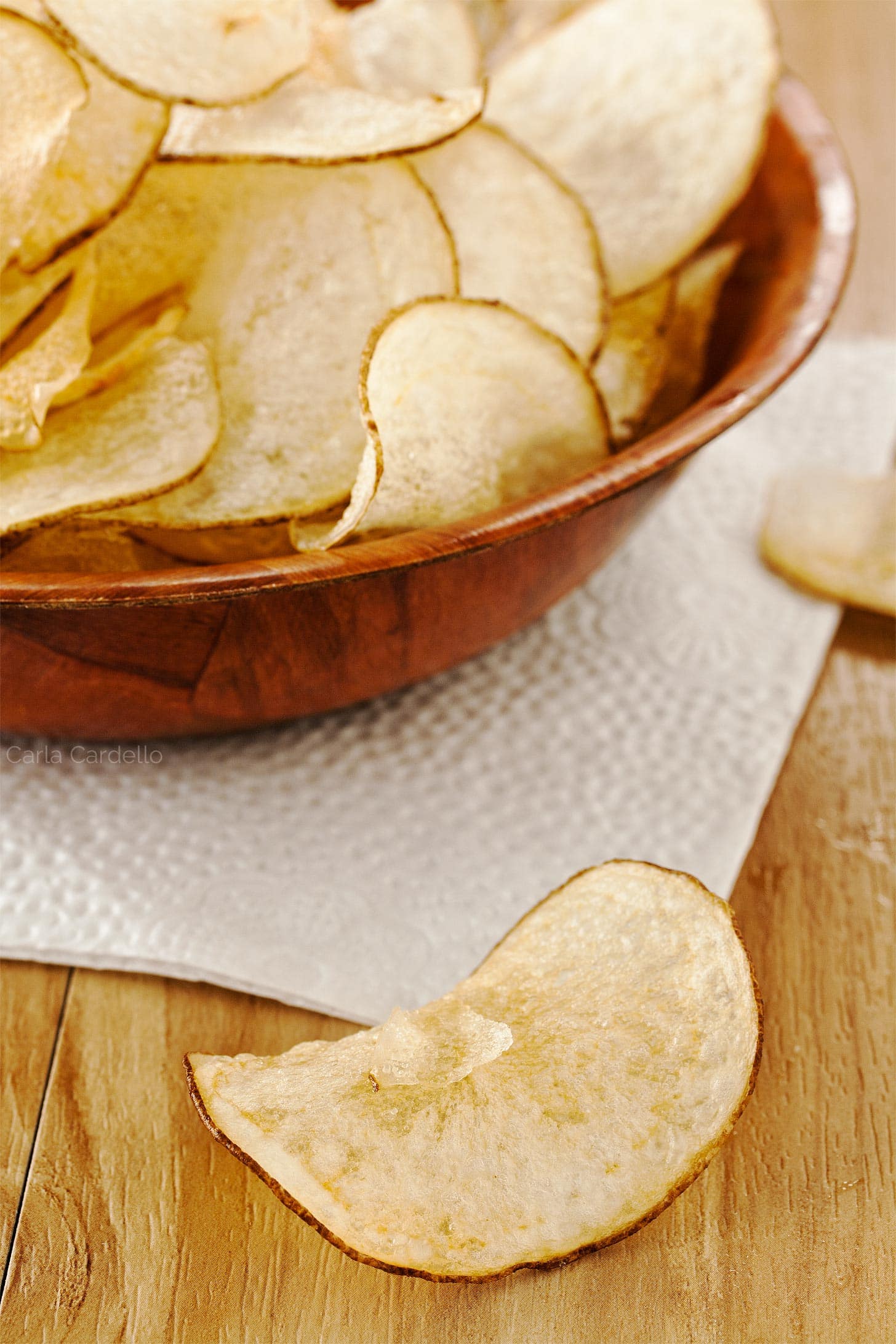 Single salt and vinegar chip next to brown bowl of chips