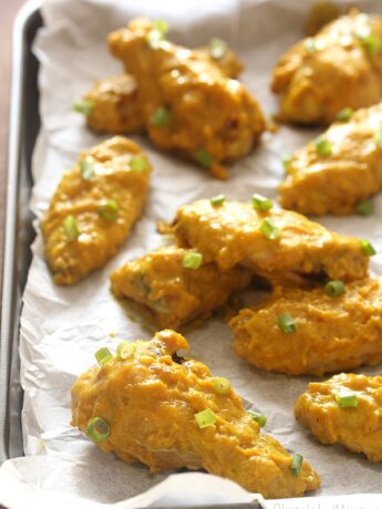 Baking tray lined with parchment paper with curry chicken wings on top