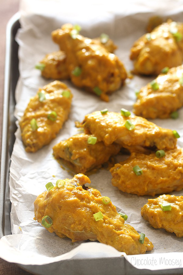 Baking tray lined with parchment paper with curry chicken wings on top