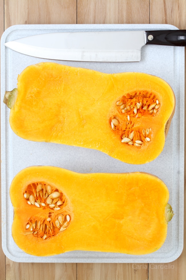 Butternut squash cut in half on a cutting board with knife