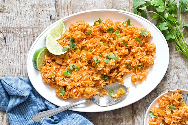 White platter of Spanish rice with spoon and small plate