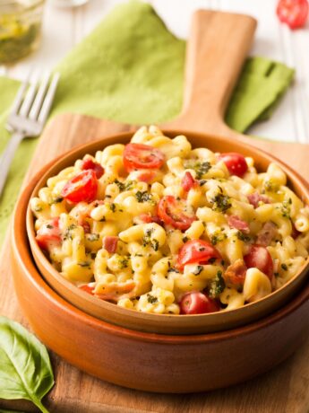 Pesto mac and cheese with bacon served in a brown bowl