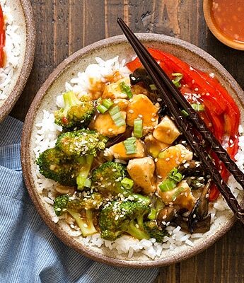 A cheaper and healthier alternative to Chinese takeout - homemade General Tso's Sweet Chili Chicken Rice Bowls with broccoli, red bell pepper, and mushrooms.