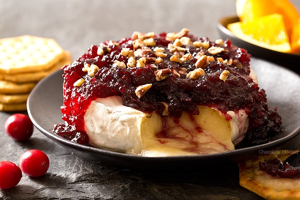 The easiest snack you can make for entertaining holiday guests - Cranberry Baked Brie served on a festive cheese board with crackers and fruit. Ooey gooey cheese ready in 10 minutes!
