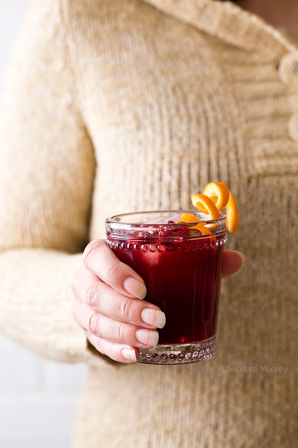 Person holding glass of pomegranate punch in hand