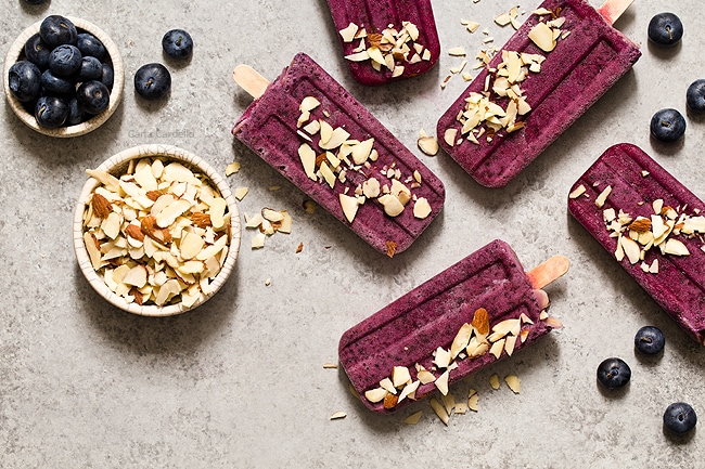 Cool down this summer with something colorful and refreshing! Blueberry Yogurt Popsicles with almonds and a secret ingredient that makes their flavor pop. 