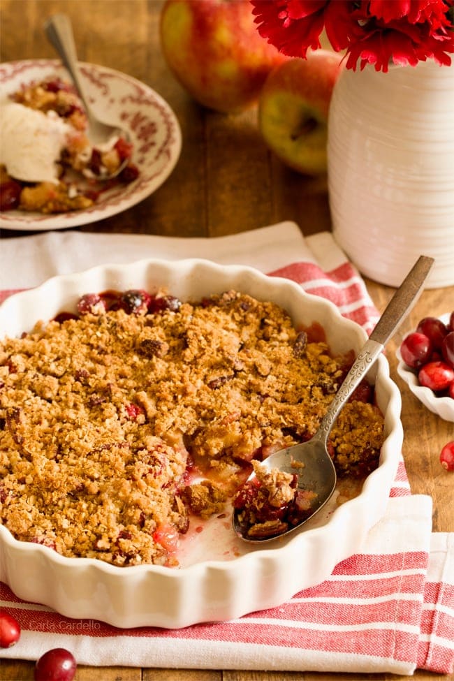 Cranberry apple crisp in white pan with a serving scooped out