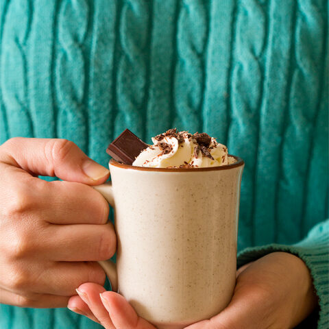 Woman in turquoise sweater holding mug of thick hot chocolate