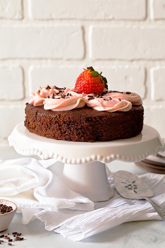 Chocolate cake with strawberry frosting on white cake stand