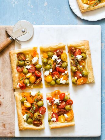 Celebrate the flavors of summer with Olive Tomato Puff Pastry Tart topped with goat cheese, thyme, and pine nuts.