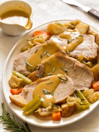 Sliced pork roast on white plate with vegetables and gravy