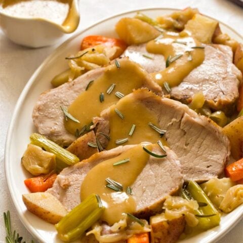 Sliced pork roast on white plate with vegetables and gravy