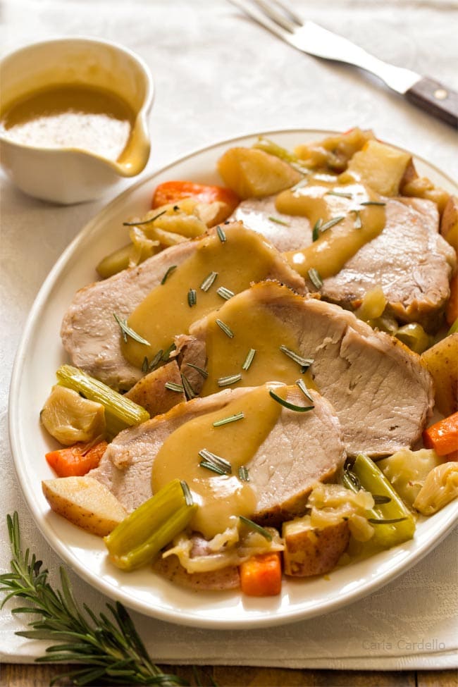 Sliced pork roast on white plate with vegetables and gravy