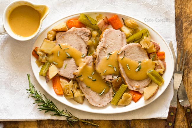 Sliced pork roast on white plate with potatoes, carrots, and gravy