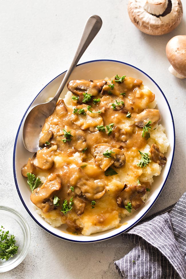 Brown mushroom gravy served over mashed potatoes on white plate