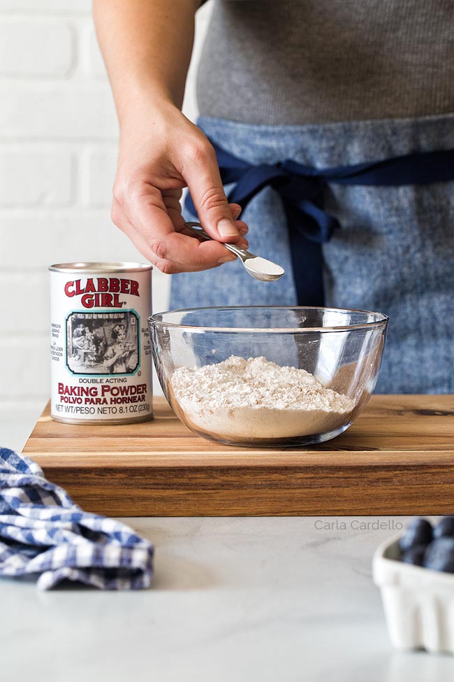 Adding half teaspoon of baking powder into a bowl of flour