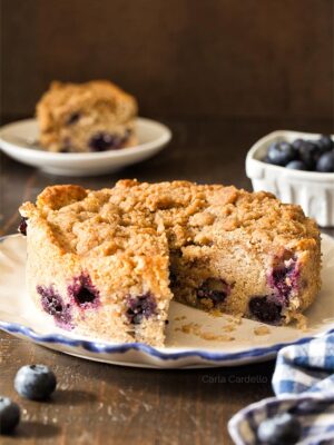 Small blueberry coffee cake on a white plate with a slice cut out