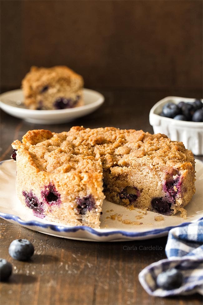 Small blueberry coffee cake on a white plate with a slice cut out