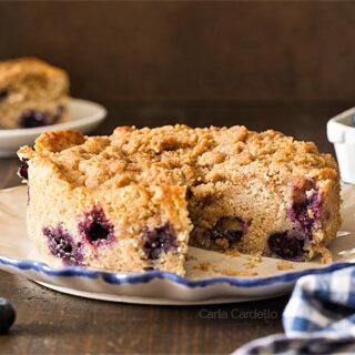 Small blueberry coffee cake on a white plate with a slice cut out