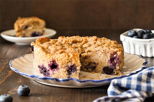 Small blueberry coffee cake on a white plate with a slice cut out