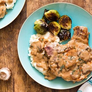 Pork chop with gravy, mashed potatoes, and Brussels sprouts on a blue plate