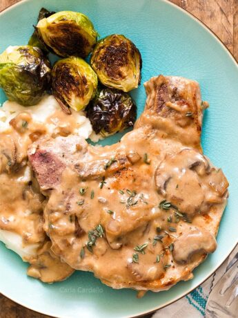 Close up of pork chop with gravy, mashed potatoes, and Brussels sprouts on a blue plate