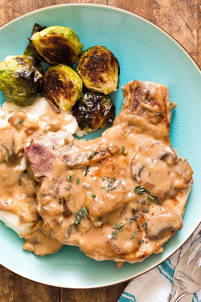 Close up of pork chop with gravy, mashed potatoes, and Brussels sprouts on a blue plate