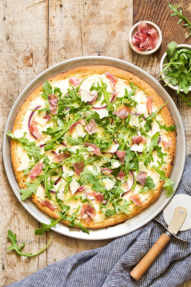 Prosciutto Arugula Pizza on a pizza pan with pizza cutter