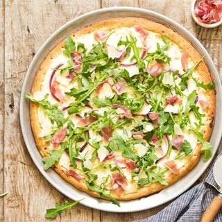 Prosciutto Arugula Pizza on a pizza pan with pizza cutter