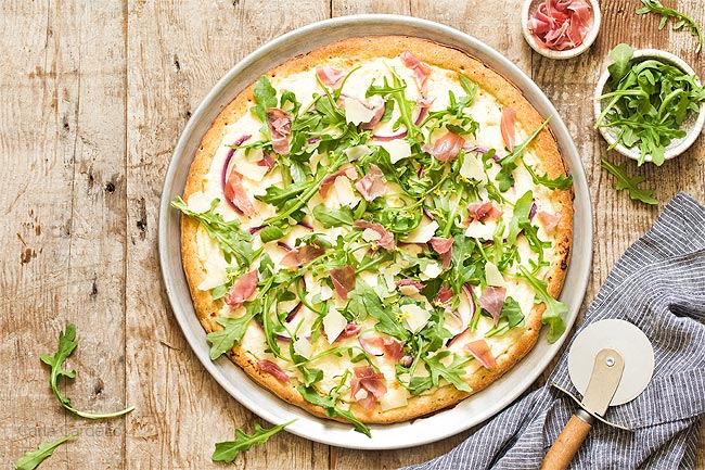 Prosciutto Arugula Pizza on a pizza pan with pizza cutter