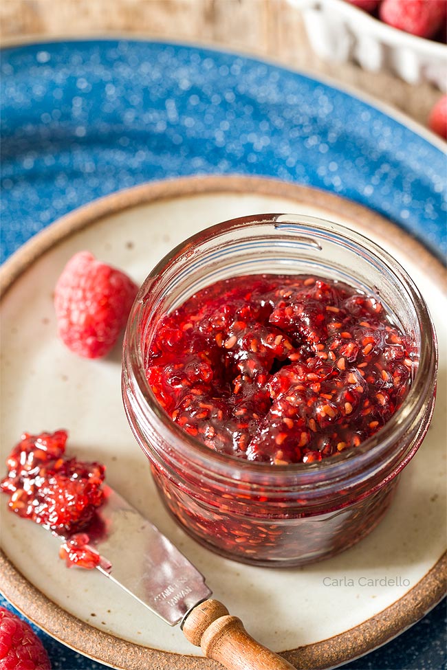 Raspberry Jam in a small jar on a plate with a knife