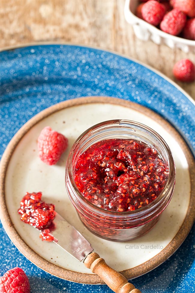 Raspberry Jam in a small jar on a plate with a knife
