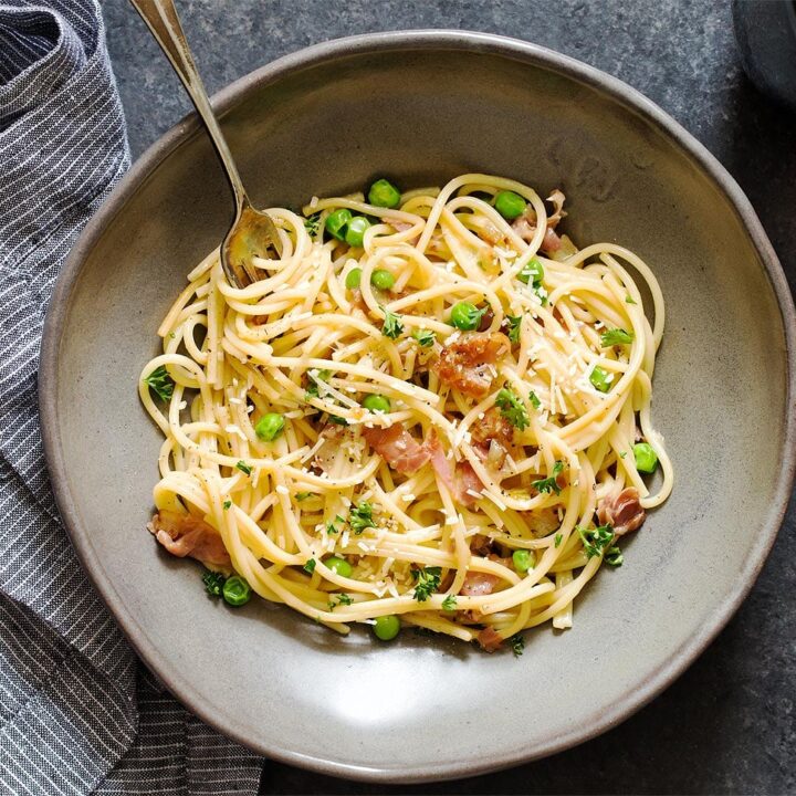 Pasta with prosciutto and peas in grey bowl with fork