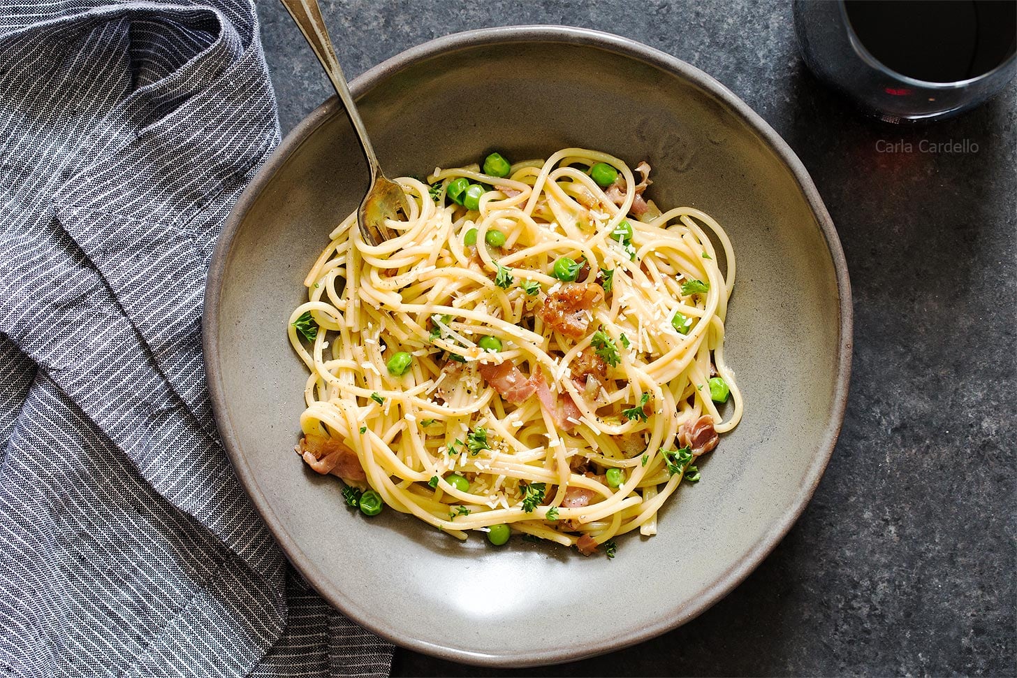 Pasta with prosciutto and peas in grey bowl with fork