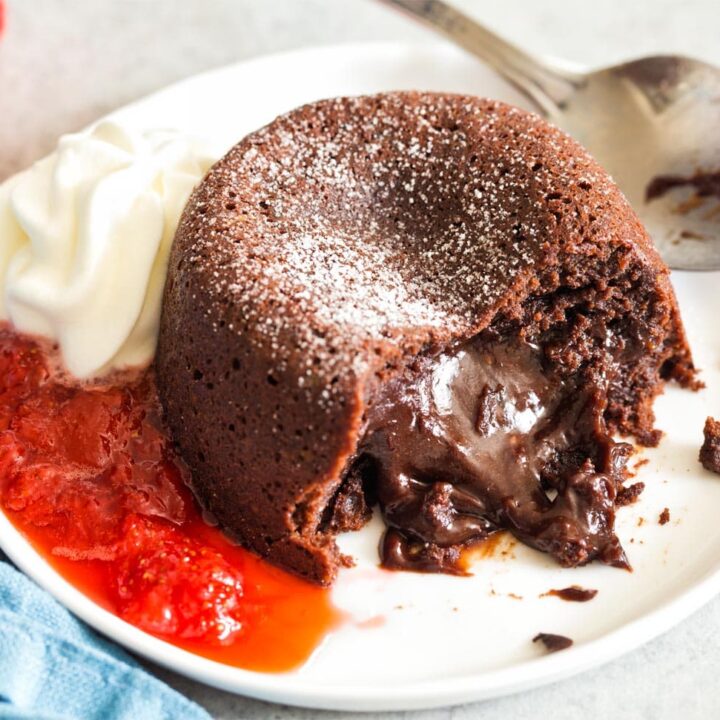 Mini Molten Chocolate Cake oozing out onto plate with whipped cream and strawberry sauce