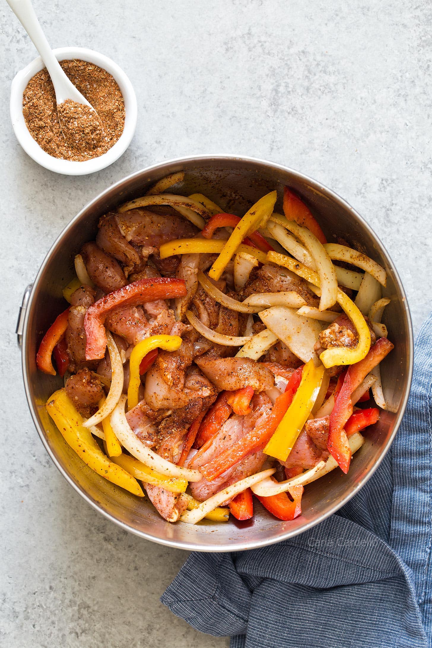 Chicken, bell pepper, and onion in a bowl with oil and fajita seasoning