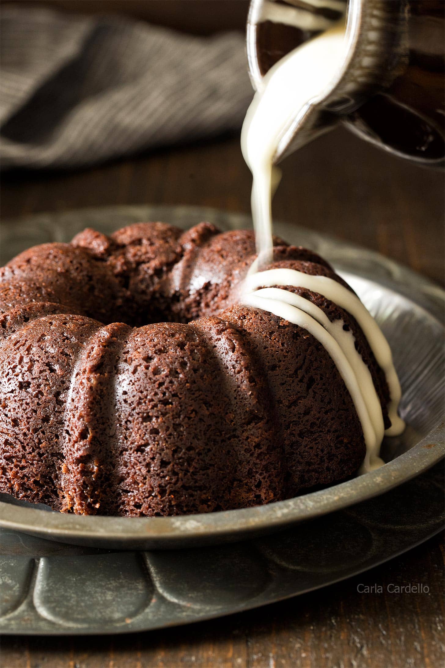 Pouring vanilla glaze on chocolate bundt cake