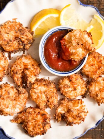 Air fryer coconut shrimp on white ruffled plate with cocktail sauce