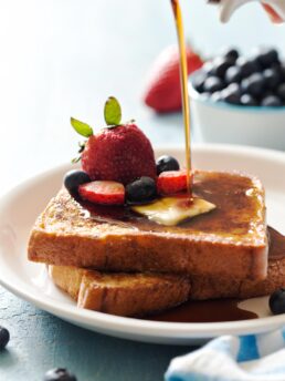 Pouring maple syrup on top of French toast for two with fresh berries