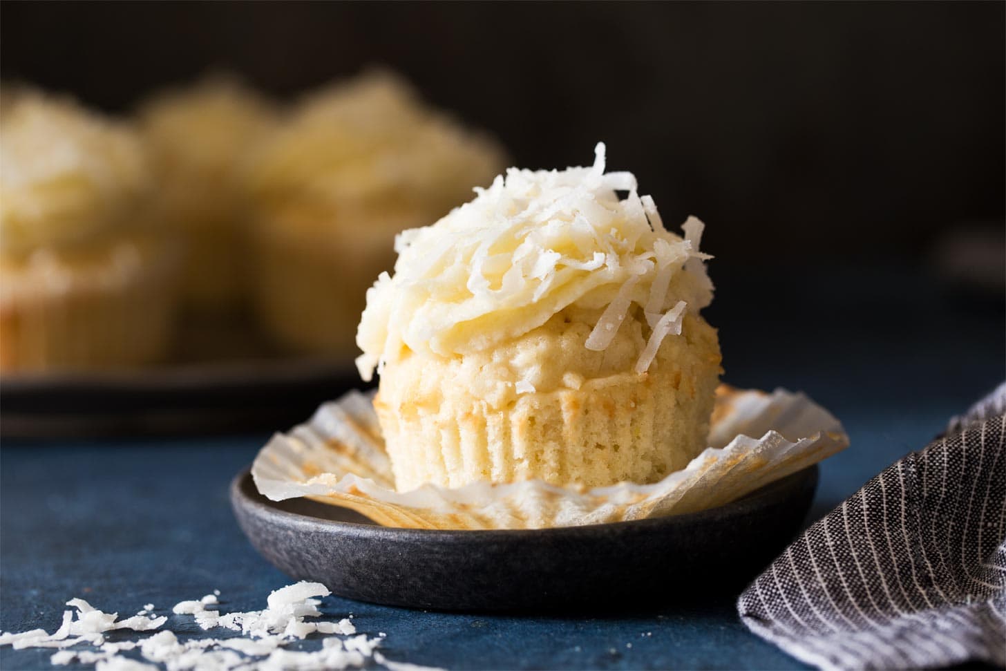 Unwrapped coconut cupcake on black plate