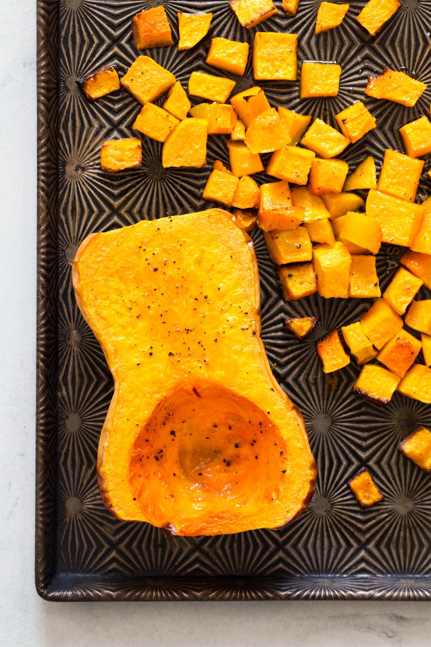 Roasted butternut squash halves and cubes on baking tray