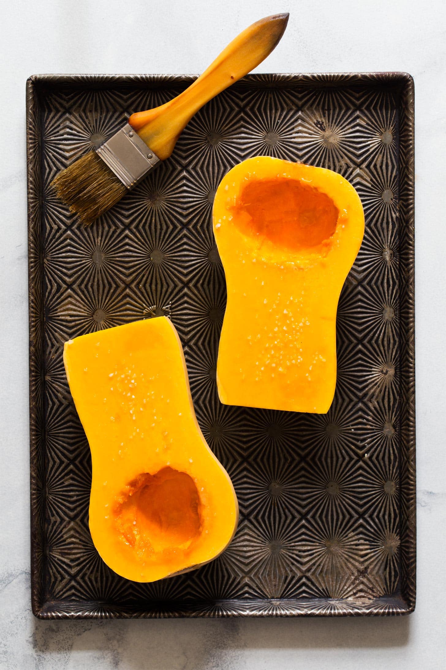 Brushing butternut squash halves with olive oil for roasting