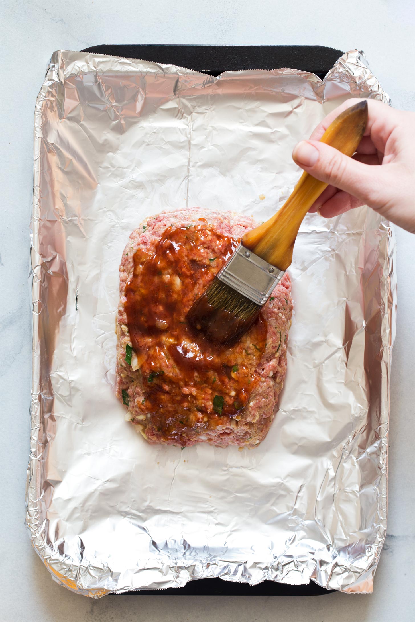 Brushing ketchup glaze on top of mini meatloaf